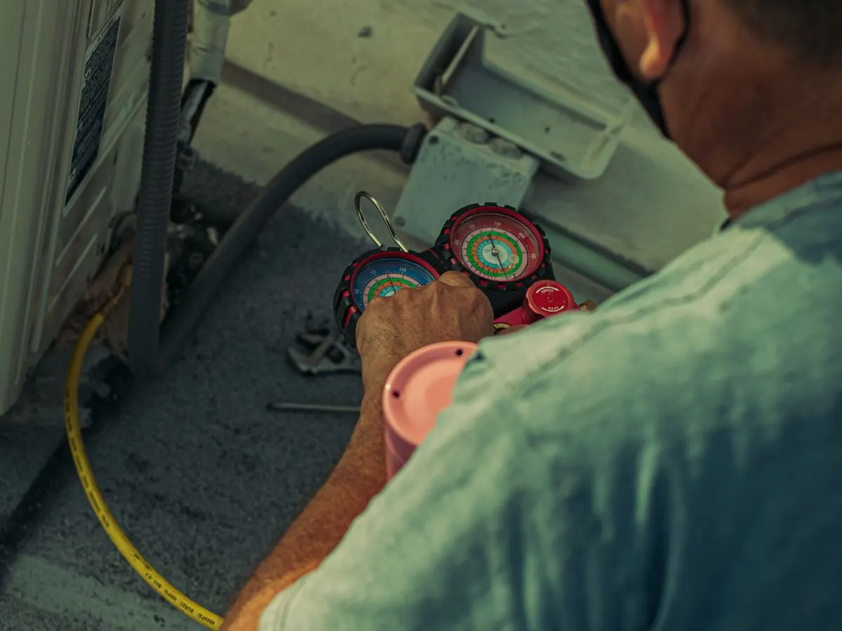 An HVAC technician checking refrigerant with manifold gauges