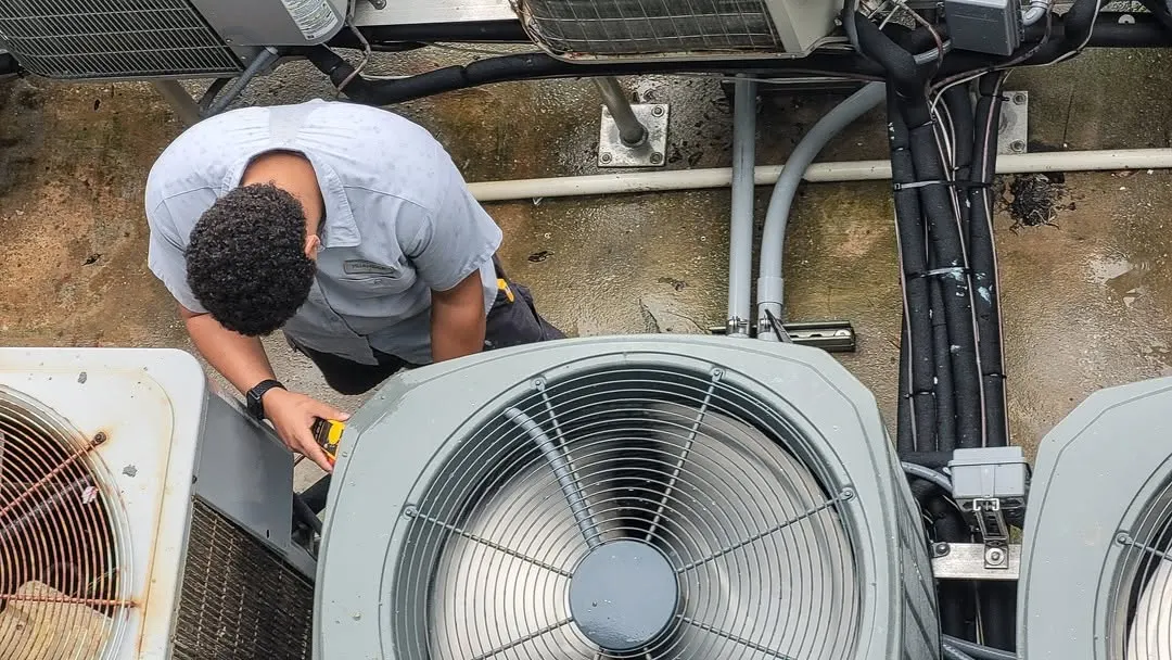 Technician servicing rooftop condenser fan units from above